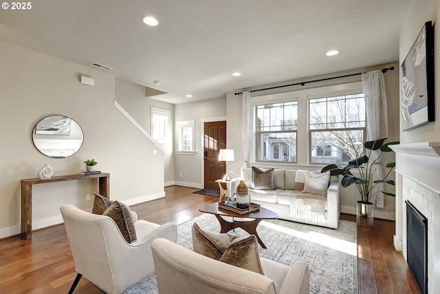 living room featuring a tile fireplace, visible vents, recessed lighting, and wood finished floors