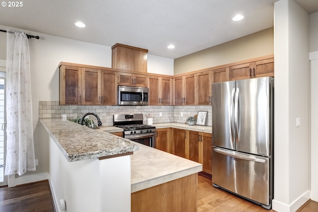 kitchen with stainless steel appliances, light countertops, a peninsula, and tasteful backsplash