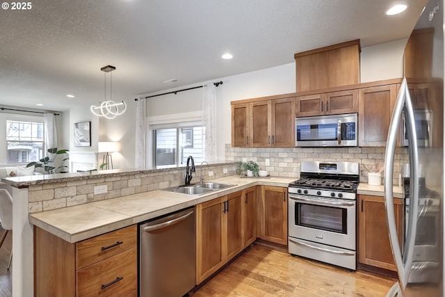 kitchen featuring backsplash, appliances with stainless steel finishes, brown cabinetry, a sink, and a peninsula