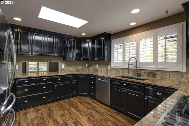 kitchen featuring appliances with stainless steel finishes, a sink, dark cabinetry, dark wood finished floors, and a skylight