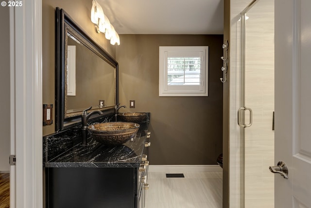 full bathroom with double vanity, a sink, baseboards, and a stall shower