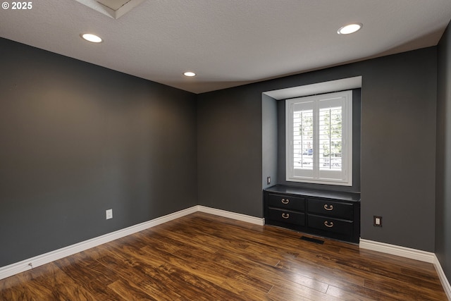 spare room with a textured ceiling, recessed lighting, baseboards, visible vents, and dark wood-style floors