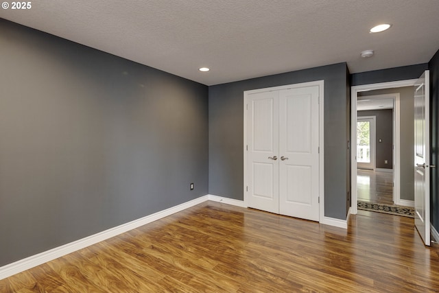 unfurnished bedroom with a textured ceiling, baseboards, wood finished floors, and a closet