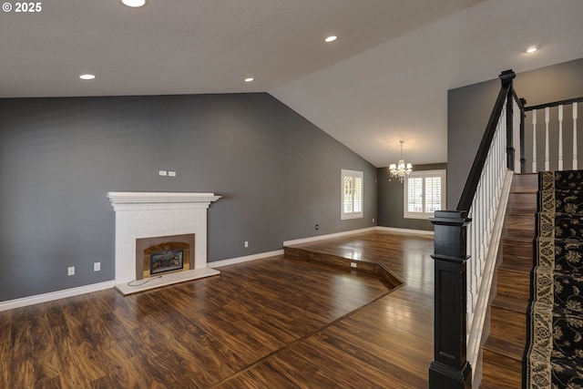 unfurnished living room featuring a notable chandelier, a brick fireplace, wood finished floors, vaulted ceiling, and stairway