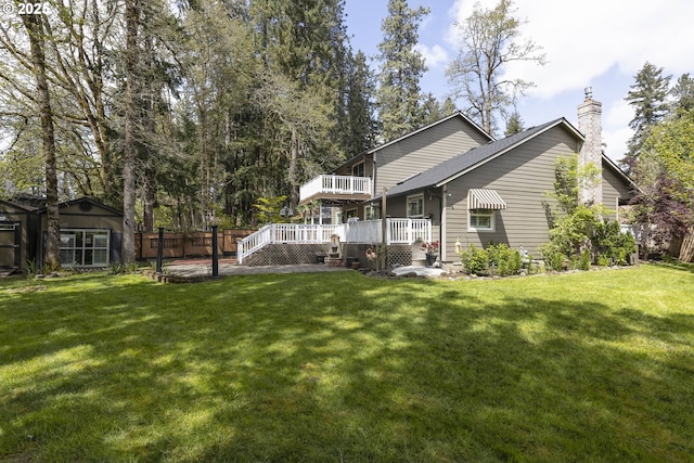 rear view of property featuring a lawn, fence, a chimney, and a deck
