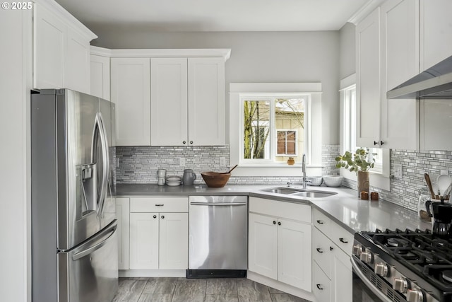 kitchen with a sink, stainless steel appliances, white cabinetry, and wall chimney range hood