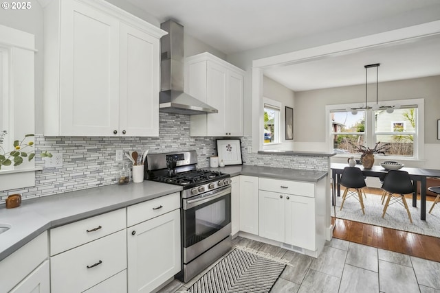 kitchen featuring backsplash, white cabinetry, a peninsula, wall chimney range hood, and stainless steel range with gas stovetop