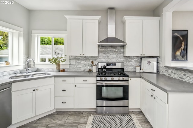 kitchen with a sink, appliances with stainless steel finishes, wall chimney exhaust hood, and white cabinetry