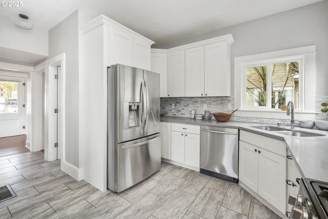 kitchen with wood tiled floor, a sink, white cabinets, appliances with stainless steel finishes, and tasteful backsplash