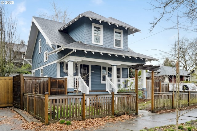 view of front of property featuring a porch, a fenced front yard, and roof with shingles