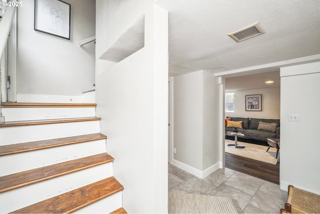 staircase featuring tile patterned flooring, baseboards, visible vents, and a textured ceiling