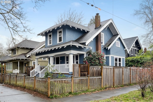 view of front of house with a fenced front yard, roof with shingles, a porch, and a chimney