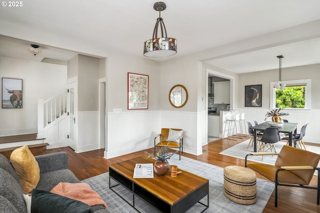 living area with a wainscoted wall, wood finished floors, and stairs