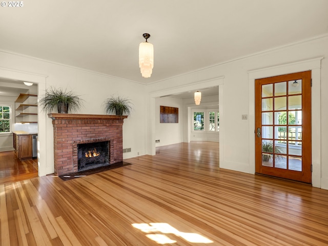unfurnished living room with light wood-type flooring, a brick fireplace, and crown molding