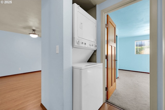 laundry room featuring baseboards, stacked washing maching and dryer, and wood finished floors