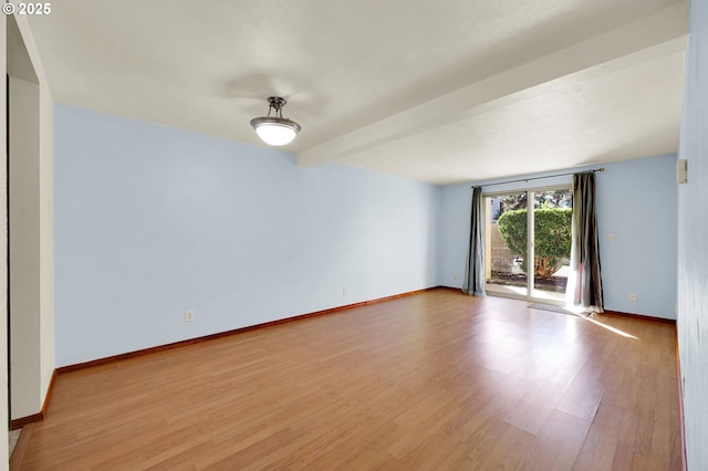 spare room with beam ceiling, baseboards, and wood finished floors