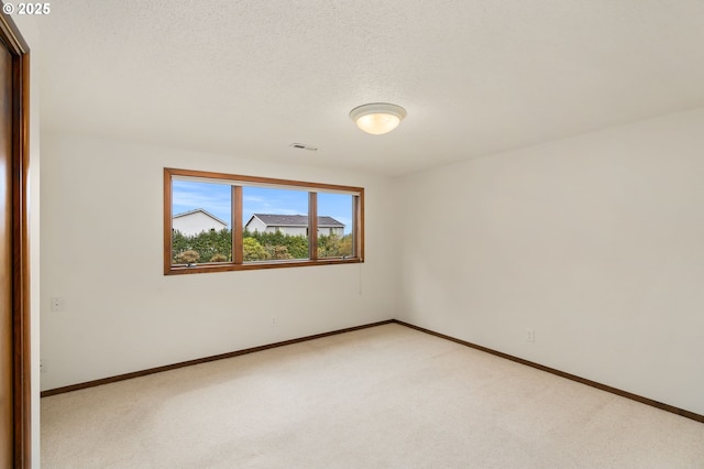 empty room featuring baseboards, light carpet, a textured ceiling, and visible vents