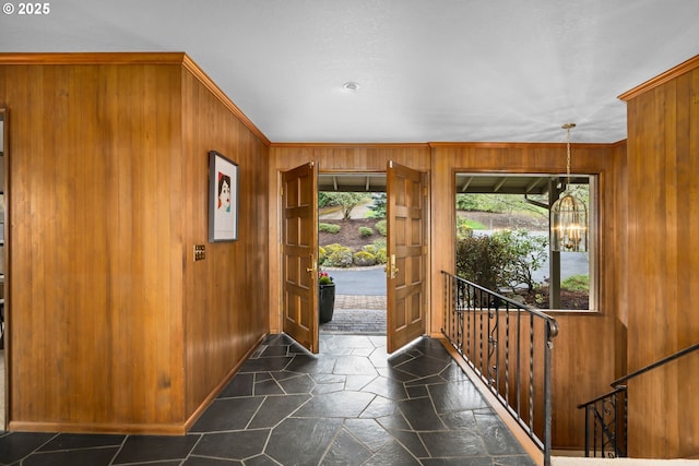 foyer entrance featuring crown molding, a notable chandelier, wood walls, and stone finish flooring