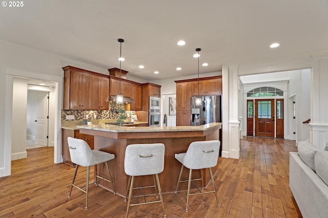 1734 NW Saltzman Rd, Portland, OR 97229 - kitchen featuring under cabinet range hood, appliances with stainless steel finishes, wood-type flooring, brown cabinets, and recessed lighting