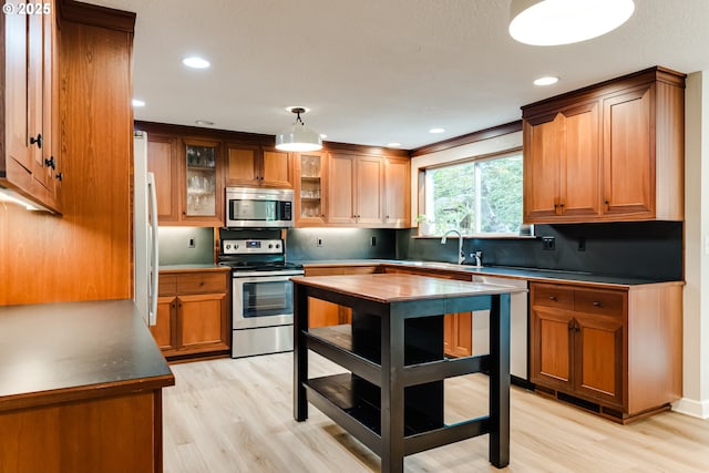 kitchen featuring light wood-style floors, brown cabinetry, tasteful backsplash, and appliances with stainless steel finishes