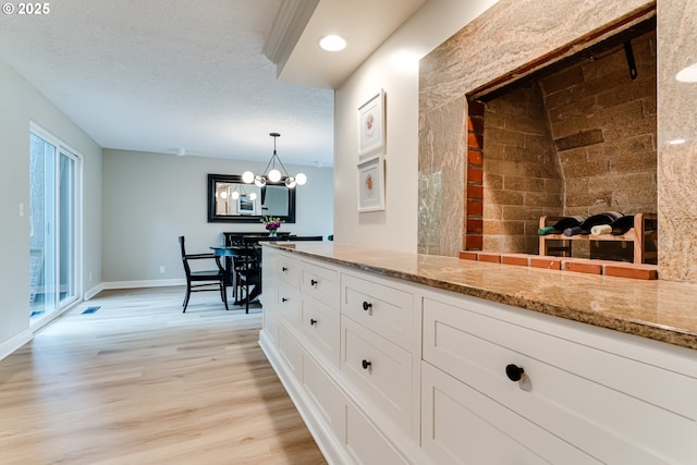 interior space featuring an inviting chandelier, light wood-type flooring, white cabinetry, baseboards, and light stone countertops