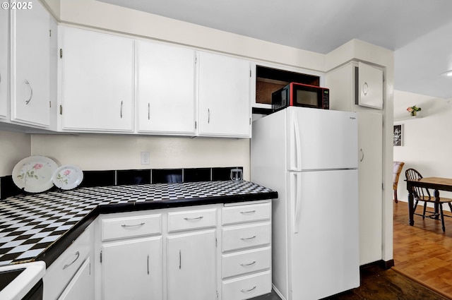 kitchen with dark wood-type flooring, tile countertops, white cabinets, and white appliances