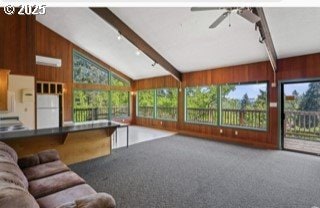 carpeted living area with wood walls, lofted ceiling with beams, and ceiling fan