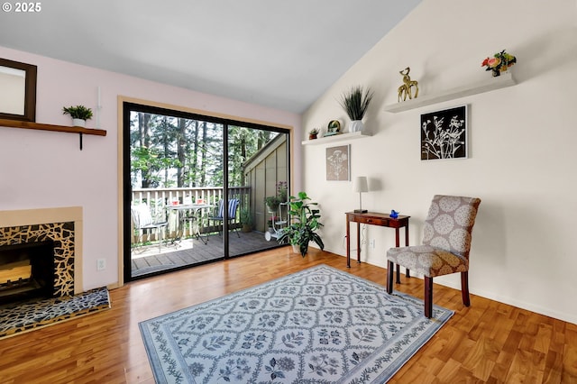 sitting room with a tiled fireplace, wood finished floors, and lofted ceiling