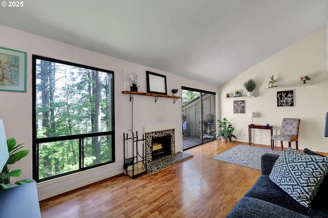 living area with baseboards, a fireplace with raised hearth, vaulted ceiling, and wood finished floors
