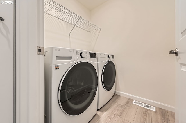 clothes washing area with washer and dryer and light hardwood / wood-style floors