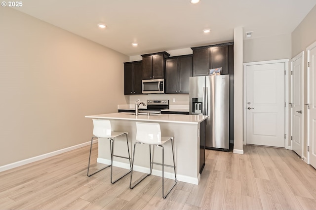 kitchen with light wood-type flooring, a center island with sink, stainless steel appliances, a breakfast bar, and sink