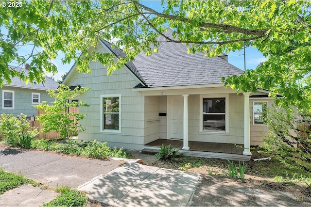 view of front of home with roof with shingles, a porch, and fence