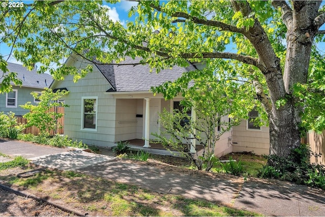 bungalow-style home with a shingled roof and fence