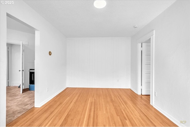 unfurnished room featuring light wood-type flooring, a textured ceiling, and baseboards