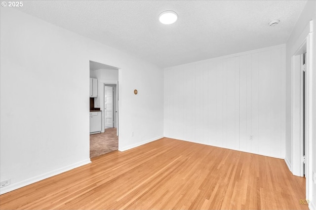 empty room with light wood-style floors, a textured ceiling, and baseboards