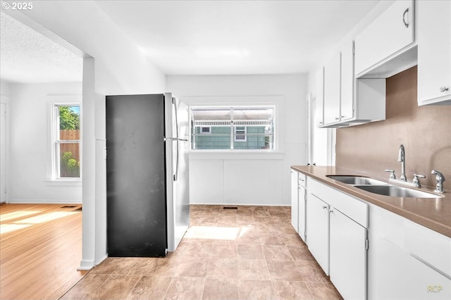 kitchen featuring freestanding refrigerator, a sink, and white cabinets