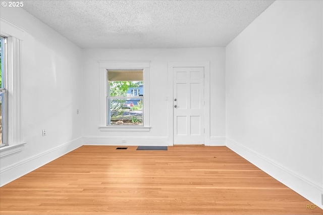 unfurnished room featuring a textured ceiling, light wood finished floors, and baseboards