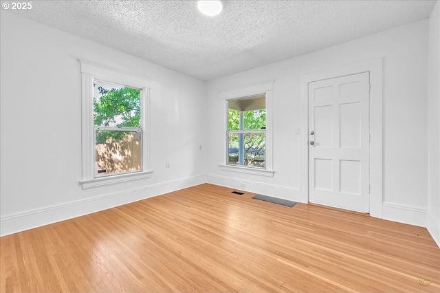 spare room with a textured ceiling, light wood-style flooring, and baseboards
