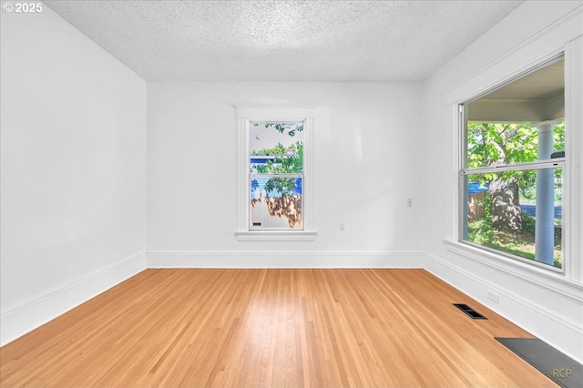 unfurnished room featuring light wood-type flooring, a textured ceiling, and baseboards