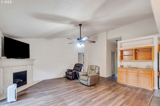 living room with visible vents, ceiling fan, vaulted ceiling, light wood-style floors, and a high end fireplace