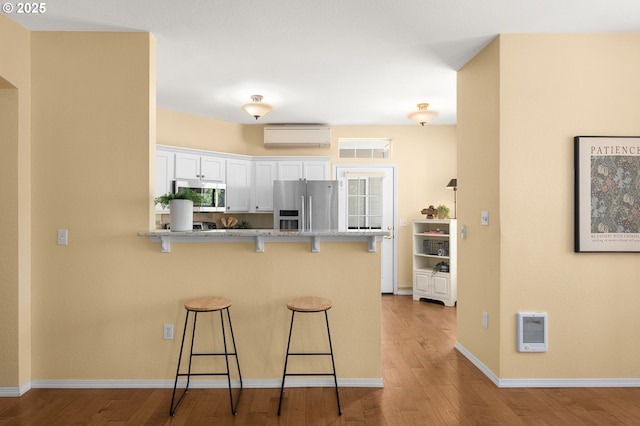 1231 NE Horizon Loop Unit 203, Hillsboro, OR 97124 - kitchen with appliances with stainless steel finishes, a wall mounted air conditioner, a kitchen breakfast bar, white cabinets, and wood finished floors