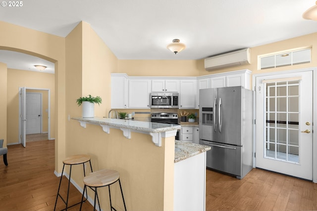 1231 NE Horizon Loop Unit 203, Hillsboro, OR 97124 - kitchen featuring stainless steel appliances, an AC wall unit, a breakfast bar, light wood-style flooring, and white cabinets