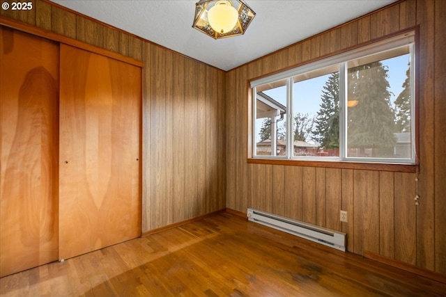 unfurnished bedroom with hardwood / wood-style flooring, a baseboard heating unit, wooden walls, and a closet