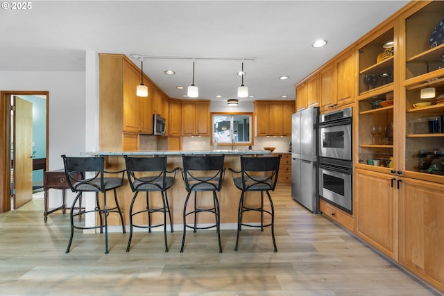 8747 S Heinz Rd, Canby, OR 97013 - kitchen with appliances with stainless steel finishes, a peninsula, light wood-style flooring, brown cabinets, and a kitchen breakfast bar
