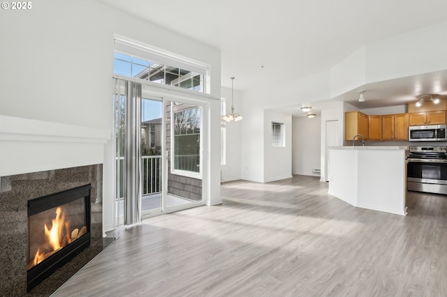unfurnished living room featuring baseboard heating, a sink, a fireplace, a chandelier, and light wood-style flooring