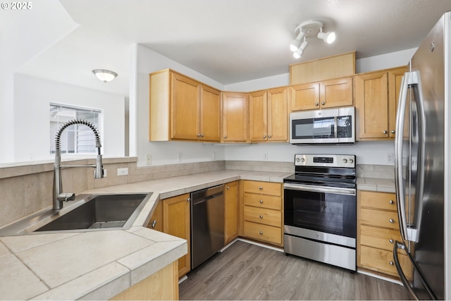 kitchen with tile countertops, wood finished floors, a sink, light brown cabinets, and stainless steel appliances
