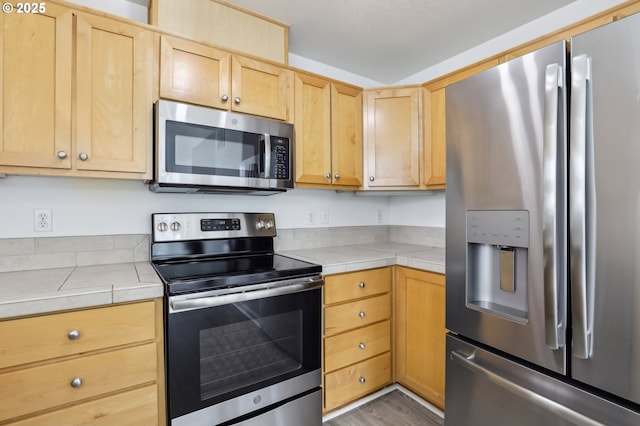 kitchen with tile counters, wood finished floors, light brown cabinets, and stainless steel appliances