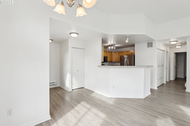 interior space featuring freestanding refrigerator, baseboard heating, light countertops, light wood finished floors, and a notable chandelier
