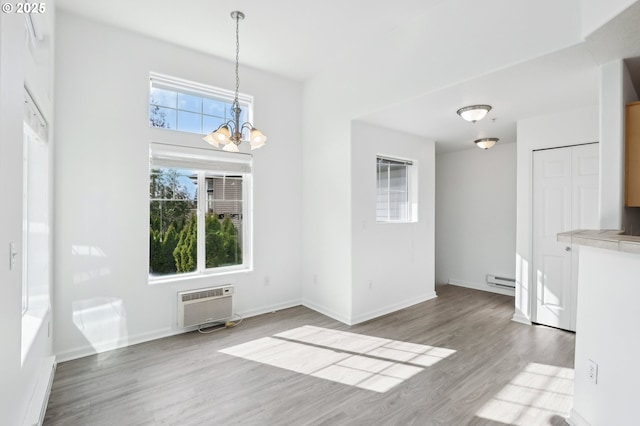 unfurnished dining area with a notable chandelier, a wall mounted air conditioner, baseboards, wood finished floors, and a baseboard radiator