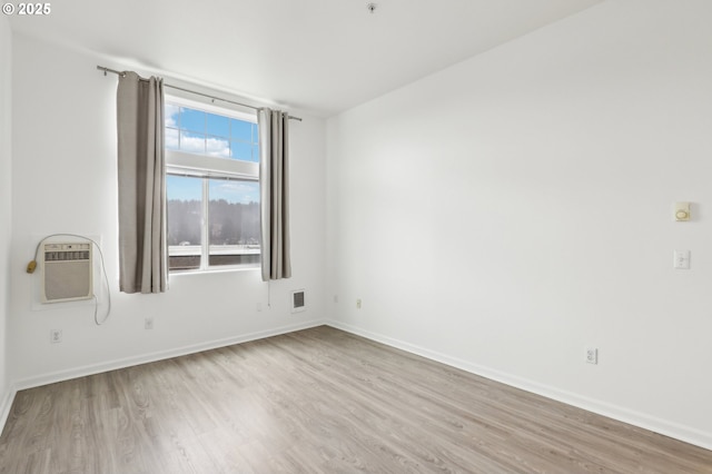 unfurnished room featuring baseboards, wood finished floors, and a wall mounted air conditioner